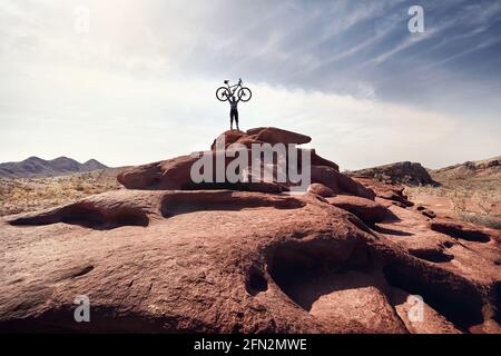 Rider with beard holding his mountain bike in silhouette in the desert volcanic mountain at national park Altyn Emel in Kazakhstan. Extreme Sport and Stock Photo