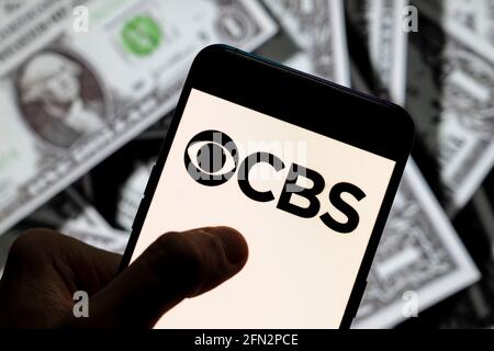 In this photo illustration the American English language commercial broadcast television and radio network CBS logo seen displayed on a smartphone with USD (United States dollar) currency in the background. Stock Photo