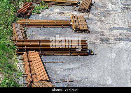 Long and thick, rust-covered steel bars stacked outside on a gravel square, viewed from above. Stock Photo