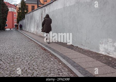 man in a hooded black jacket walking on the street Stock Photo