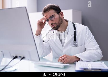 Frustrated Overworked Doctor In Hospital Looking At Computer Stock Photo