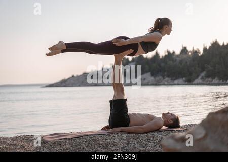 couple doing flying superman yoga pose on the beach acro yoga concept 2fn309j
