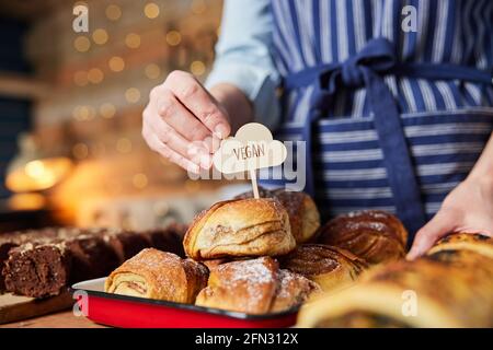 Sales Assistant In Bakery Putting Vegan Label Into Freshly Baked Cinnamon Buns Stock Photo