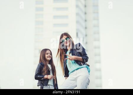 Fashion family look. Woman with child girl in family fashionable clothes having fun outdoor. Fashion young mother and child daughter wearing a sunglas Stock Photo