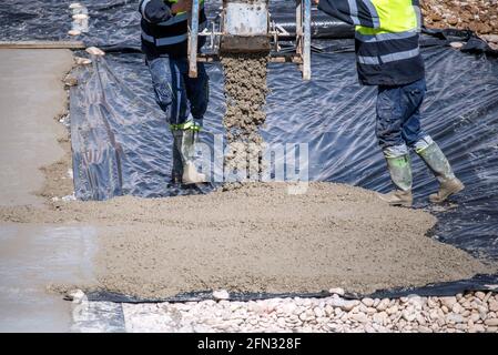 Two construction workers at work pouring a mixture on a floor with a plastic sheet. Stock Photo
