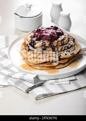 Food still life. Close-up a stack of delicious hot pancakes with chocolate and raspberry jam. Traditional delicious dessert or sweet breakfast on a wh Stock Photo
