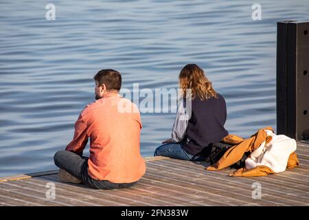 Young man and woman sitting on jetty or pier by the sea Stock Photo