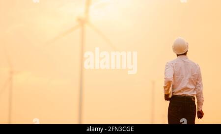 African engineer windmills wearing white hard hat and using tablet with   wind turbine on silhouette sunset Stock Photo
