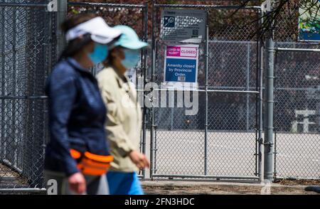 Toronto, Canada. 13th May, 2021. People wearing face masks walk past closed public tennis courts in Toronto, Ontario, Canada, on May 13, 2021. Ontario, Canada's most populous province, announced on Thursday to extend the provincewide stay-home-order against COVID-19 for two more weeks till early June. Credit: Zou Zheng/Xinhua/Alamy Live News Stock Photo