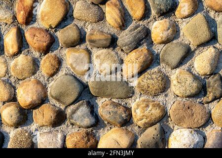 pebble stones lie in rows partially pressed into the main surface of the wall, road or floor Stock Photo