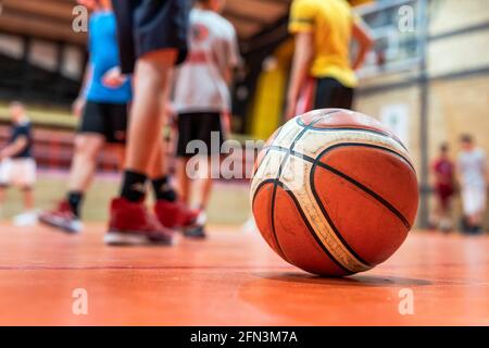 Basketball ball on the floor in sport gym on the court selective focus with blurred feet of unknown children on training sport and development concept Stock Photo