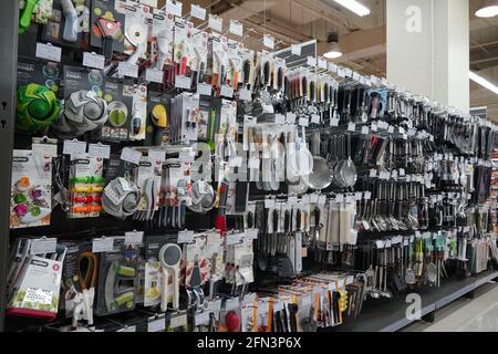 Kitchen Tools Hanging In Shop. Large Set And Variety Of Different Manufacturers On Shelves In Store. Kitchenware, Knives, Spatulas, Ladle, Tongs, Spoo Stock Photo