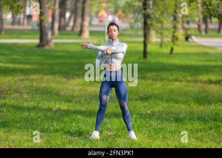 Young woman stretching shoulders - warming up before running or working out. Female runner stretching arms before running at morning. Fitness and heal Stock Photo