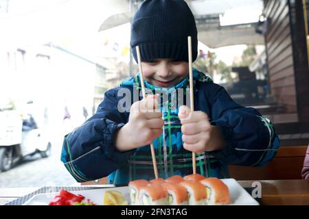 Boy taking sushi with chopsticks on restaurant terrace Stock Photo