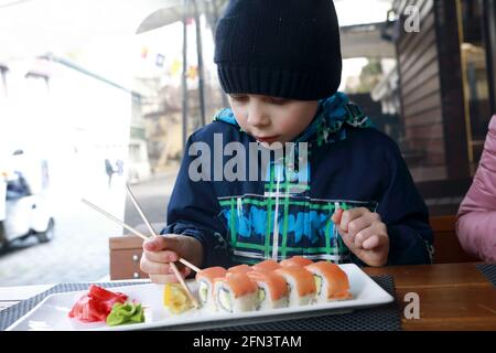 Child taking sushi with chopsticks on restaurant terrace Stock Photo