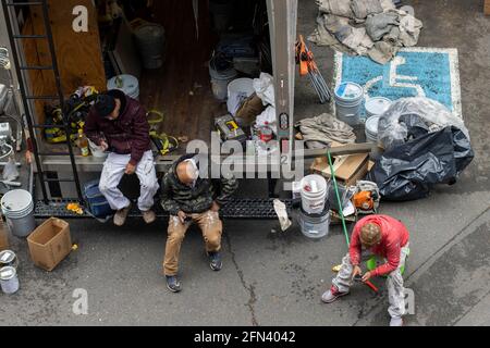 Three latino workers from a painting company use their mobile phones while taking a break and sitting at the back of their truck in a neighborhood ... Stock Photo