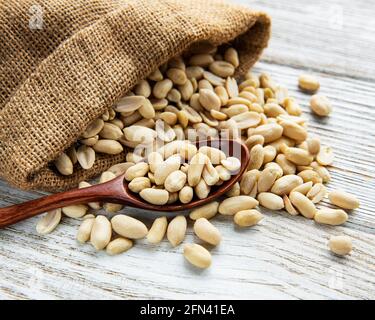 Peeled peanuts in a burlap bag on a white wooden background Stock Photo