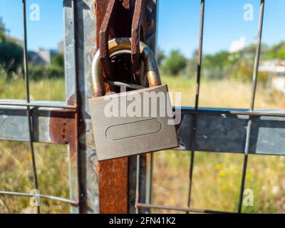 Privacy and protection of property concept. Rusty old padlock locked on gate of metal grid fence. Entrance forbidden, security safety, industry factor Stock Photo