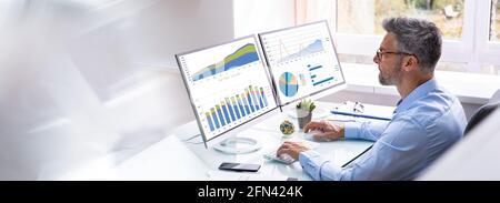 Man Advisor Using Multiple Computer Monitors With Finance Charts Stock Photo
