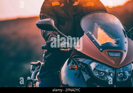 Motorbiker holding steering bar, riding in beautiful sunset. Travel and freedom, outdoor activities concept. Stock Photo