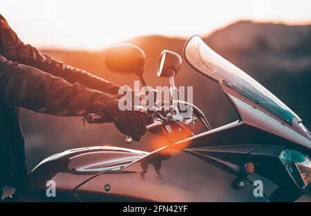 Motorbiker holding steering bar, riding in beautiful sunset. Travel and freedom, outdoor activities concept. Stock Photo