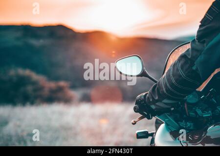 Motorbiker holding steering bar, riding in beautiful sunset. Travel and freedom, outdoor activities concept. Stock Photo