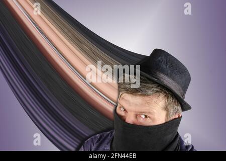 Middle-aged man wearing black hat with small brim and scarf over his face. Male hides his face behind the buff. Unrecognizable Person on blue backgrou Stock Photo