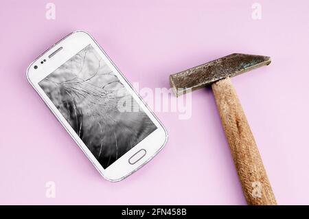A cell phone with smashed LCD screen and a hammer on purple background Stock Photo