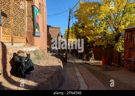 Male resident sitting against a wall and enjoying the autumn sun in the ancient village Abyaneh, Isfahan Province, Iran Stock Photo