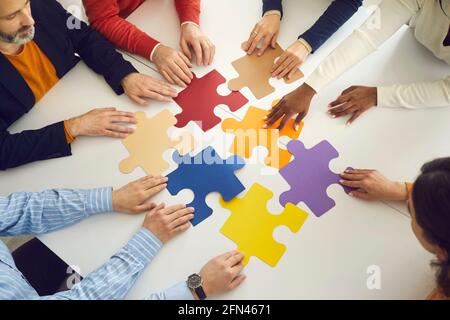 Multinational teammate people group hand moving puzzle pieces on office table Stock Photo