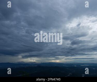 A view of a large mountain under gloomy clouds with raining in distant sky background cloudy wallpaper Stock Photo