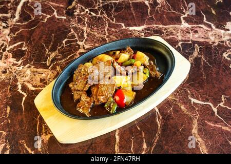 Asian style beef meal with savory sauce and some vegetables mixed in, sitting on a hot plate beneath a marbled surface. Stock Photo