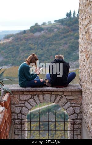 Teens seated on an arch. New technologies and ancient architectures. Teenagers use their mobile phones outdoors. Stock Photo