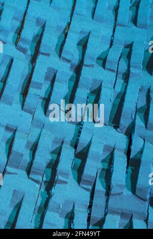 Industrially shredded cardboard packaging in blue light. For recycling waste materials, eco-friendly packaging, abstract shapes, shredding evidence. Stock Photo