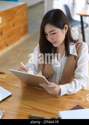 Portrait of female student using digital tablet on wooden table in co working space in library Stock Photo