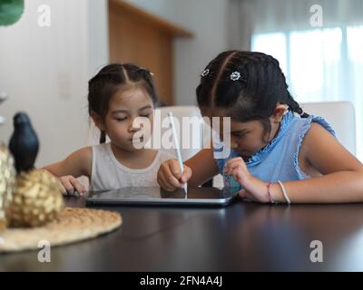 Portrait of two sisters using digital tablet together on table in living room Stock Photo