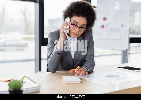 African american businesswoman talking on smartphone and using calculator Stock Photo