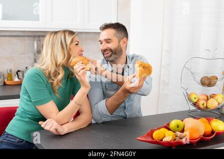 Sweet couple eats croissants for breakfast. Newlyweds eat together in the kitchen. Happiness, fruit and lifestyle. Stock Photo