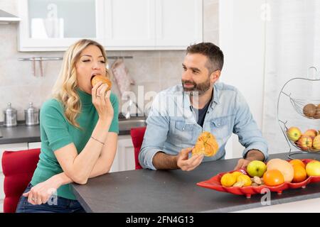 Sweet couple eats croissants for breakfast. Newlyweds eat together in the kitchen. Happiness, fruit and lifestyle. Stock Photo