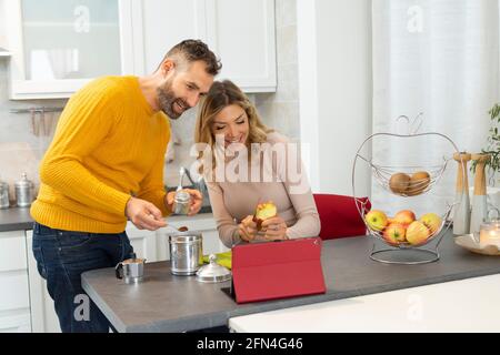 Nice couple making video call on a tablet. Newlyweds in connection with relatives during breakfast. Italian couple prepares fruit and coffee. Stock Photo