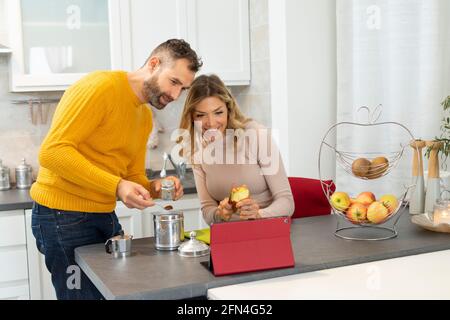 Nice couple making video call on a tablet. Newlyweds in connection with relatives during breakfast. Italian couple prepares fruit and coffee. Stock Photo