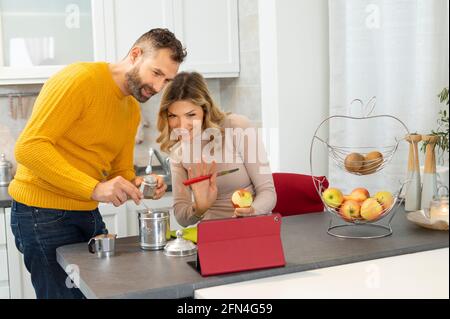 Nice couple making video call on a tablet. Newlyweds in connection with relatives during breakfast. Italian couple prepares fruit and coffee. Stock Photo