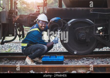 African machine engineer technician wearing a helmet, groves and safety vest is using a wrench to repair the train Stock Photo