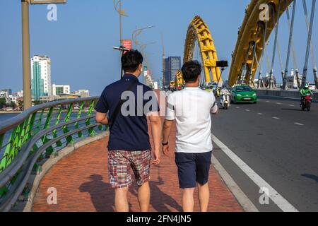 Male tourists using selfie stick walking over Dragon Bridge during day, Da Nang, Vietnam Stock Photo