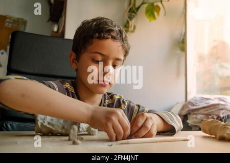 child playing with clay at home during quarantine. focused boy creating shapes with hands and using creativity and manual skills to mold toy shapes Stock Photo