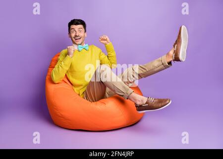 Full size photo of brunet hooray guy sit on bag wear yellow sweater trousers sneakers isolated on pastel lilac color background Stock Photo