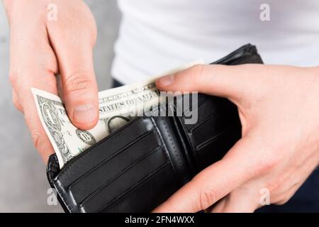 unrecognizable young man holding black leather wallet with two dollars in hands. Close up photo. Financial crisis concept. Stock Photo
