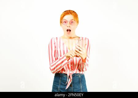 Portrait of a surprised natural redhead woman with open mouth wearing pink white stripes knot shirt & hipster cat eye sunglasses pointing finger at ce Stock Photo