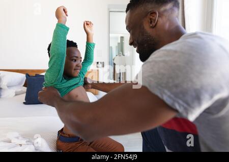 African american father and son sitting on bed, helping with dressing up Stock Photo