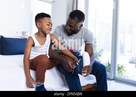 African american father and son sitting on bed, helping with dressing up Stock Photo